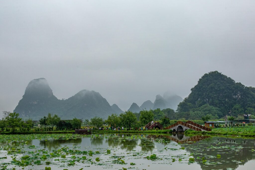 Scenic view of foggy karst mountains reflected in a calm lake with lush greenery.