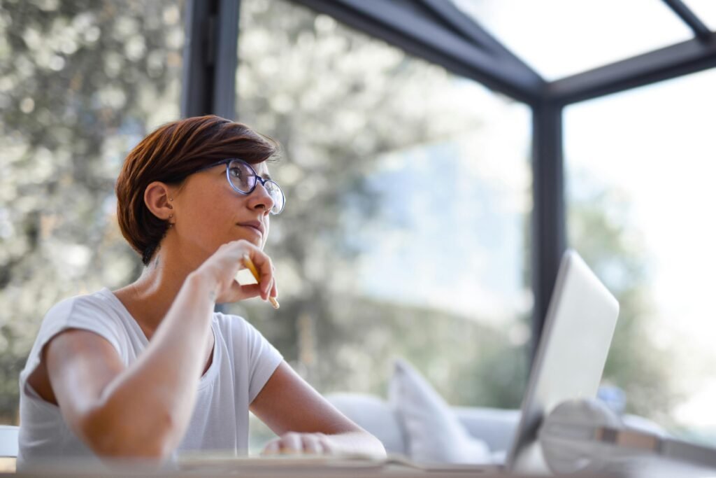 Thoughtful woman with glasses and short hair looking out window in a modern room.