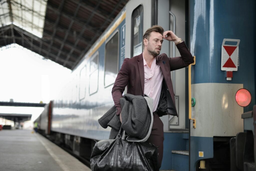 A man in a suit, carrying bags, looks stressed as he boards a train at a railway station.