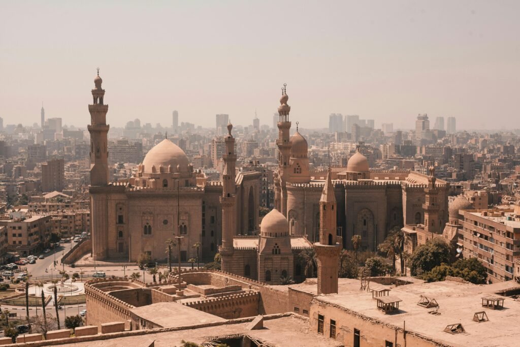 Aerial view of Cairo's historic mosques with a modern skyline backdrop under a clear sky.