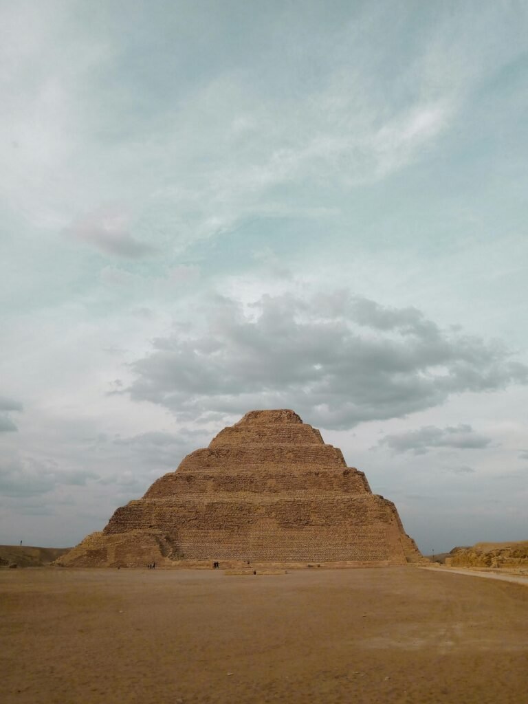 A stunning view of the ancient Step Pyramid of Djoser under a cloudy sky in Saqqara, Egypt.