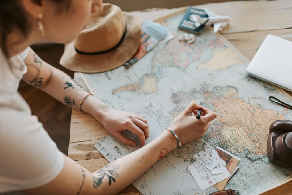 Person planning a journey with a map, passport, and travel essentials on a wooden table.