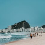 Sunny day at Copacabana Beach, Rio de Janeiro, with iconic mountains and lively crowd.